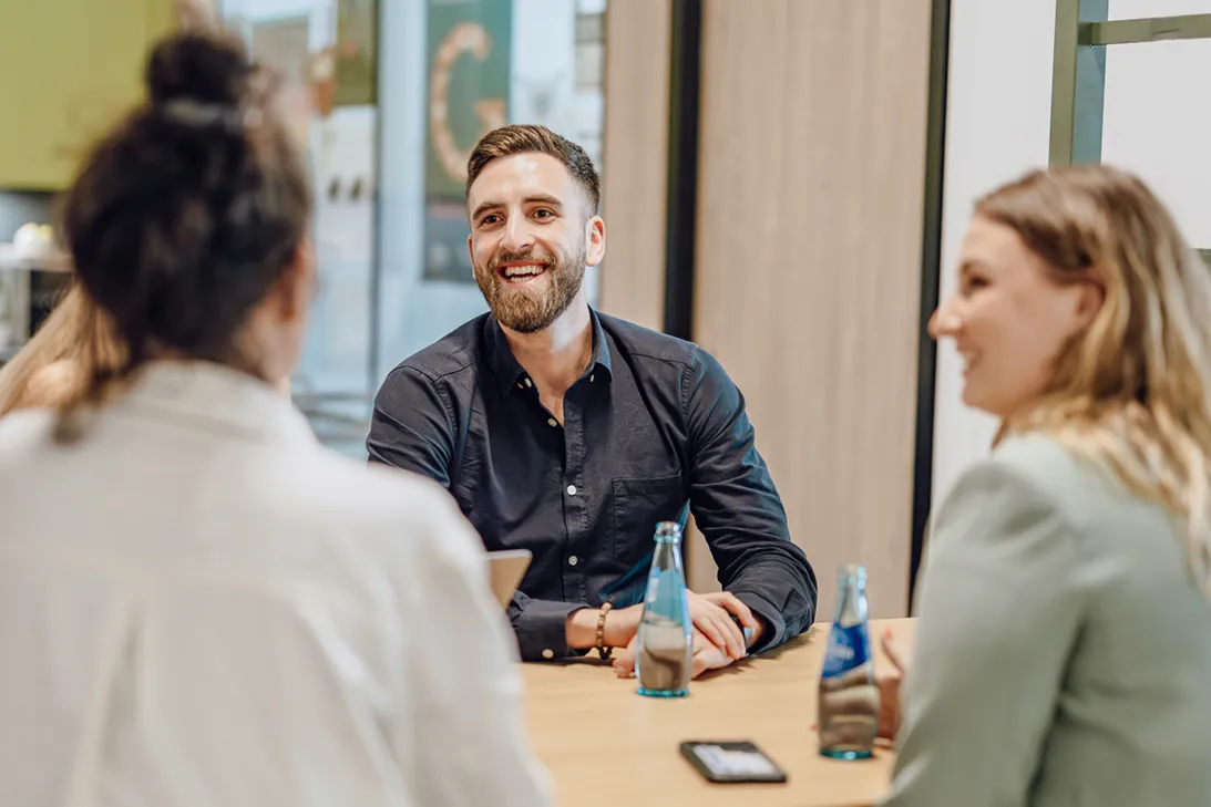 Three people sitting at a table having a friendly conversation, with water bottles and a smartphone on the table.