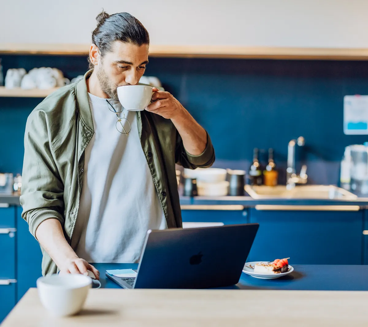 Man drinking coffee while using a laptop in a modern kitchen setting.