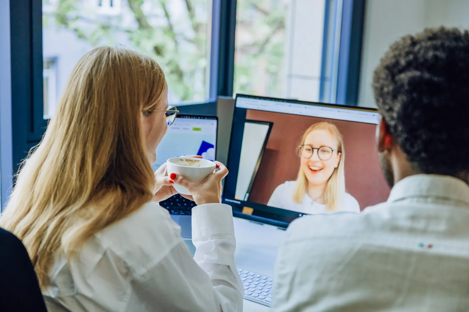 Two people having a video call on a computer screen, with one holding a coffee cup.